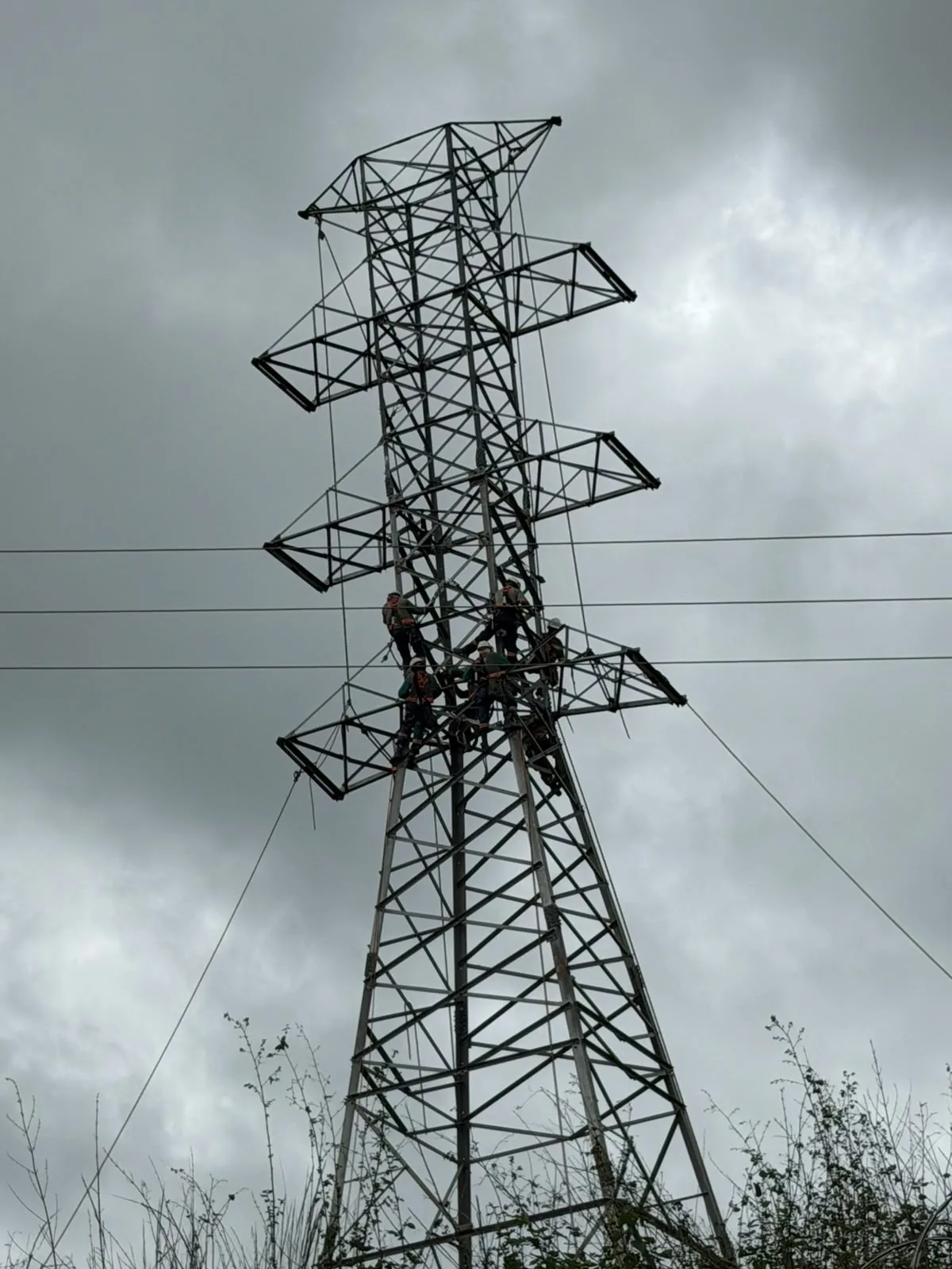 Equipe em montagem de torre de transmissão sob céu nublado