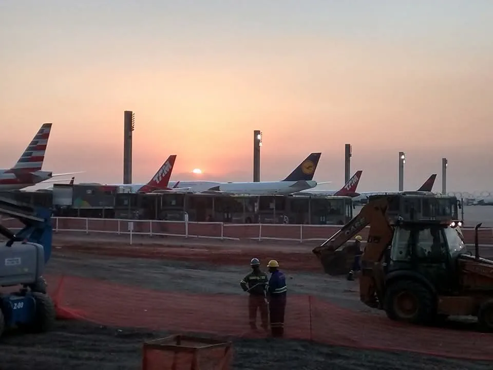 Equipe e retroescavadeira da FMC no pátio do Aeroporto do Galeão ao entardecer