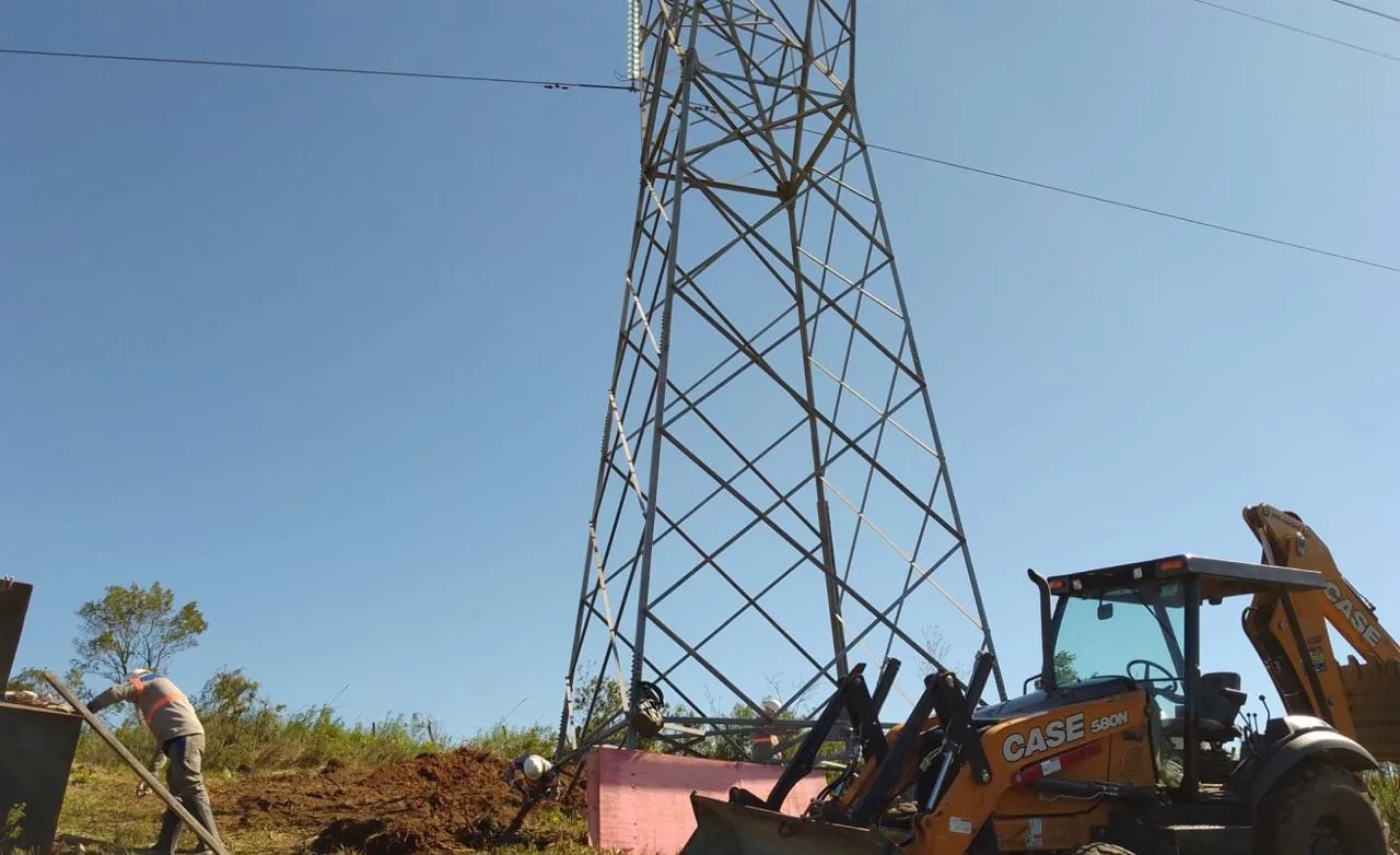 Retroescavadeira CASE e profissional escavando junto à base de uma torre de transmissão